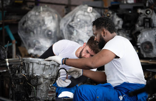 Two mechanics working on a car engine in a repair shop.