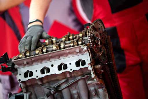 Close-up of a car engine on exhibit with a mechanic inspecting parts by hand.
