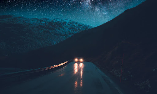A car driving on a dark mountainous highway at night with headlights illuminating the road