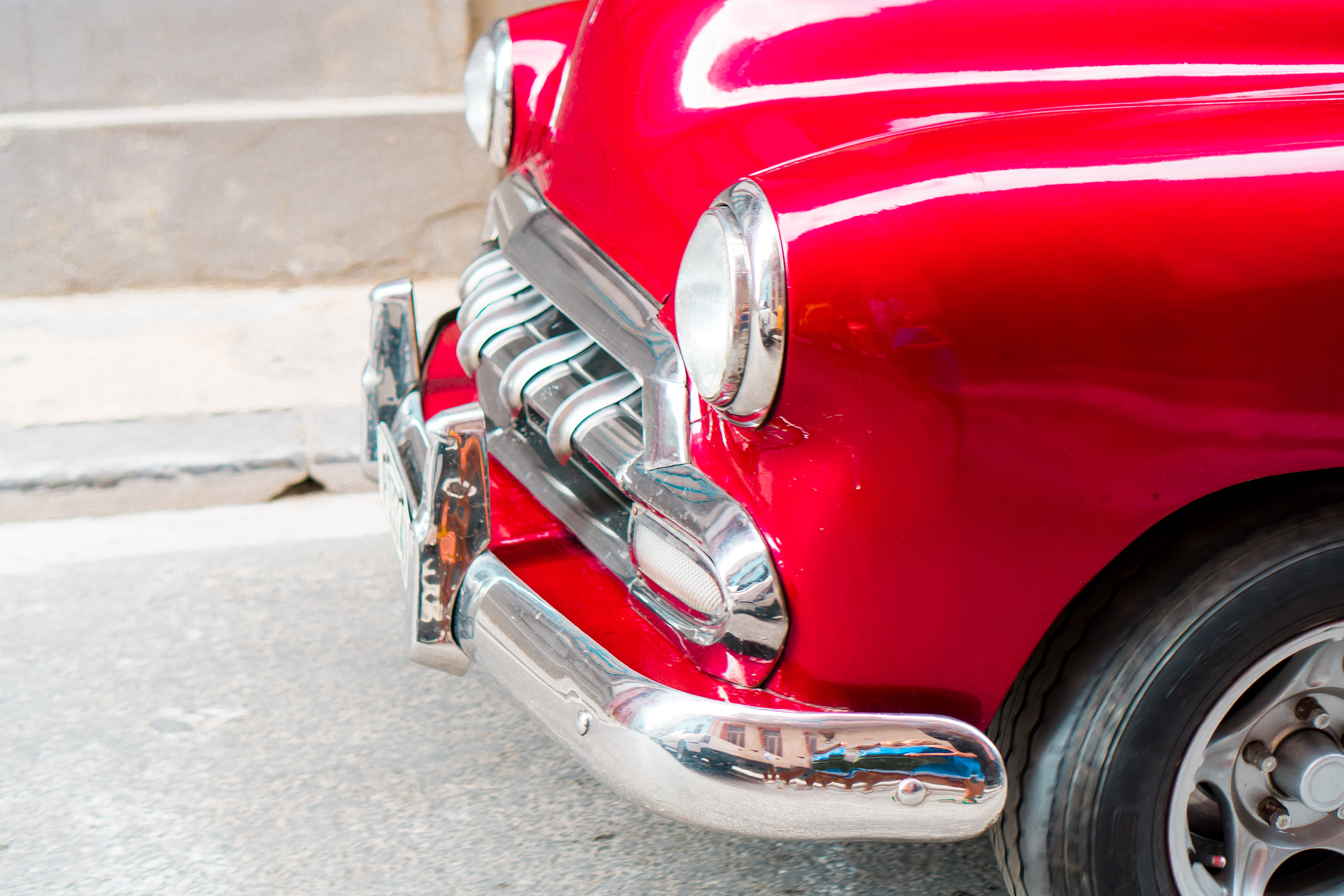 A classic red car with a silver bumper shines in the light.